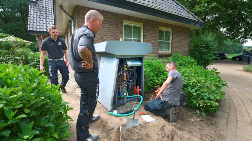 3 installatiemonteurs staan te kijken naar een warmtepomp, het kastje van de pomp staat open