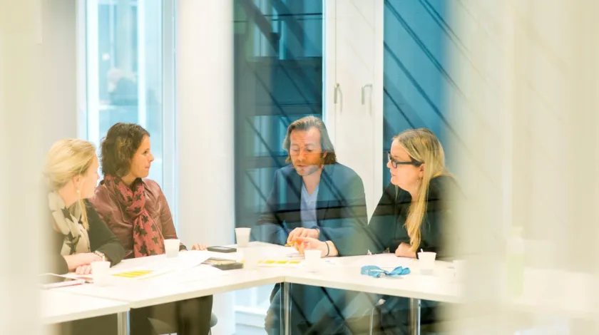 4 mensen zitten aan een witte tafel te overleggen