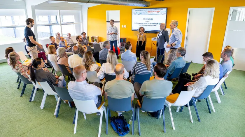 Een groep mensen zit in een halve cirkel om een viertal dat staand presenteert.