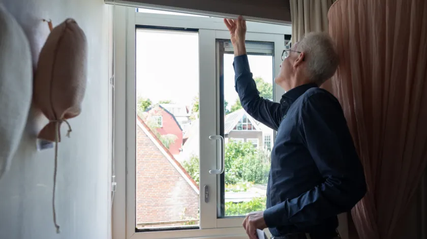 Man in raamkozijn bezig met rolgordijn