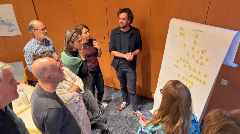 Een man staat voor een flipboard te praten tegen een groepje mensen