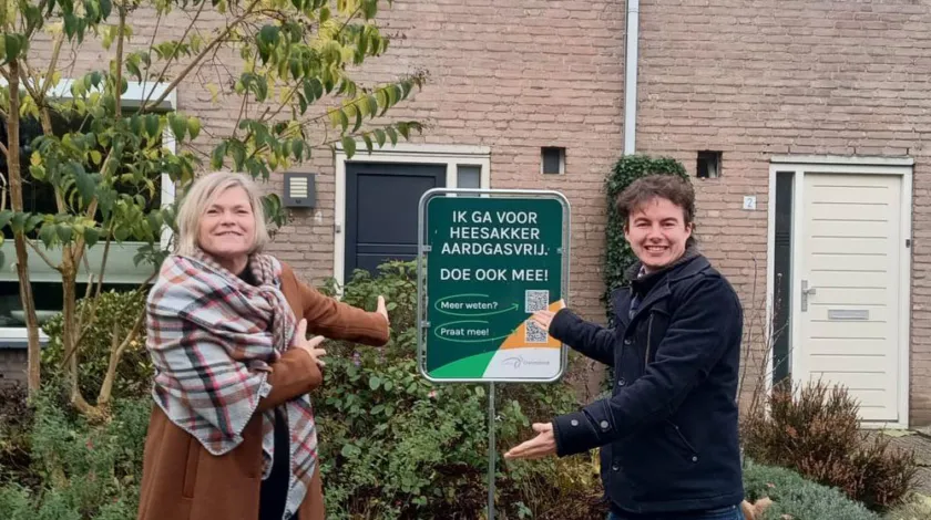 Twee bewoners wijzen trots op het bord in hun tuin, met de tekst 'Ik ga voor Heesakker aardgasvrij. Doe ook mee!'