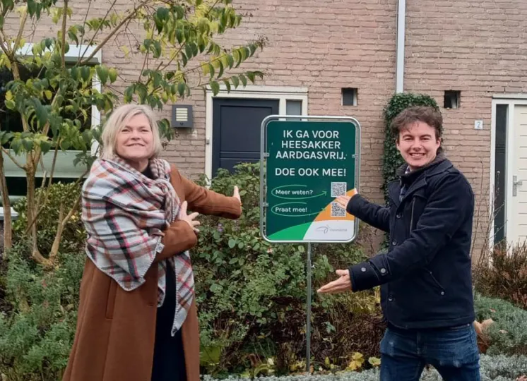 Twee bewoners wijzen trots op een bord in hun tuin, met de tekst 'Ik ga voor Heesakker aardgasvrij. Doe ook mee!'