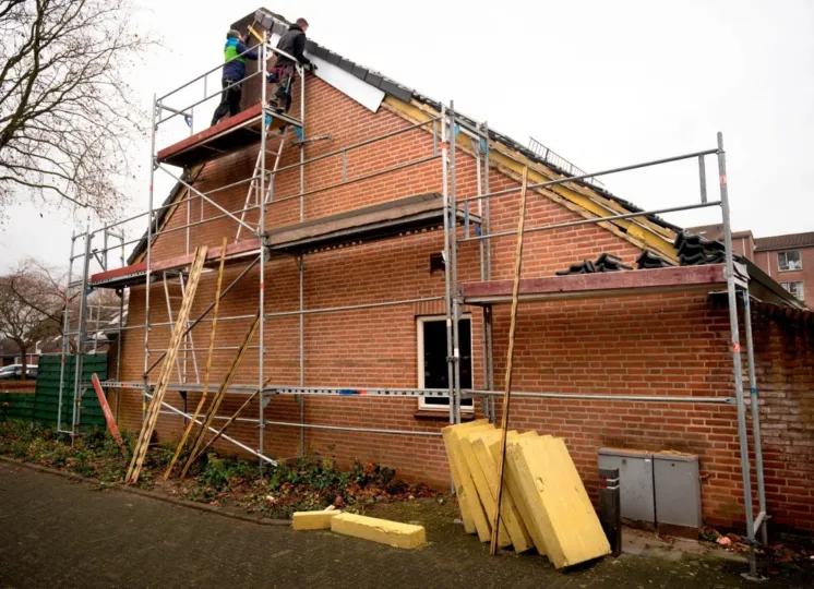 Twee mannen staan op een steiger om het dak van een hoekhuis te isoleren.
