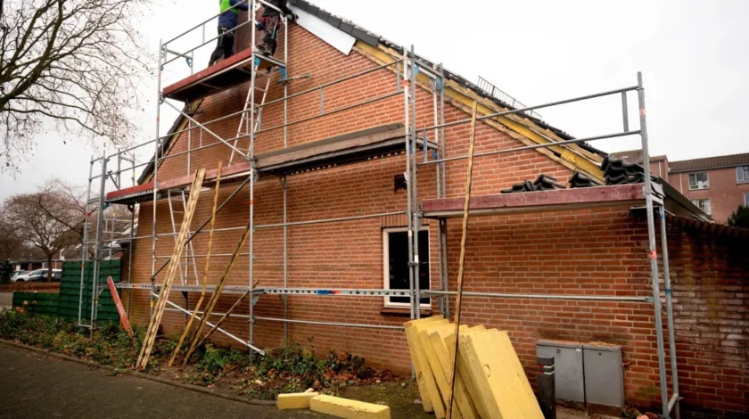 Twee mannen staan op een steiger om het dak van een hoekhuis te isoleren.