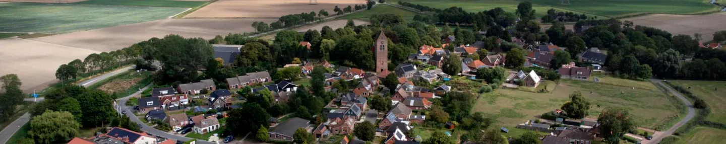 Luchtopname van boerderijen en dorpskern van Krewerd omringd door weilanden en akkers met in de verte de Eems