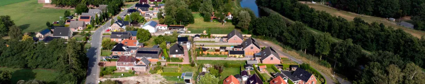 Luchtfoto van het dorp Steendam. De woonkern omzoomd door bomen, bestaat uit lintbebouwing en een kleine woonwijk met vrijstaande huizen. Op de achtergrond een uitgestrekt weide- en akkerbouwgebied met aan de horizon een groot windmolenpark