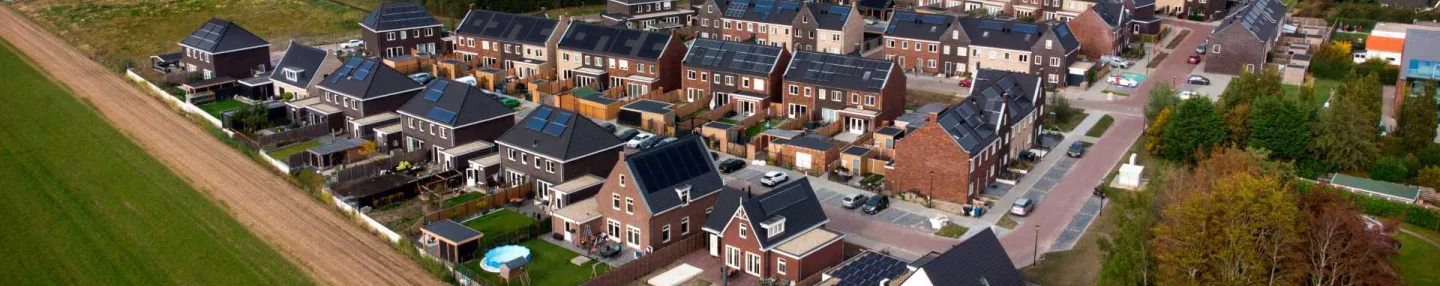 Dronebeeld van de proeftuin Van Pallandtpolder met tussen de weilanden een woonwijk met vrijstaande huizen en rijtjeshuizen voorzien van zonnepanelen. In de verte staan windmolens