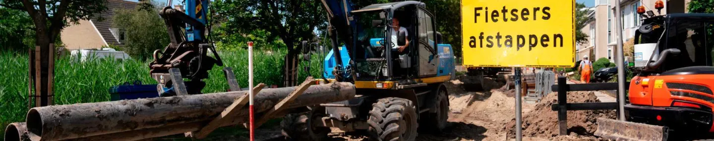 Opgebroken weg in een woonwijk. Graafmachine verplaatst buizen voor de aanleg van een warmtenet.