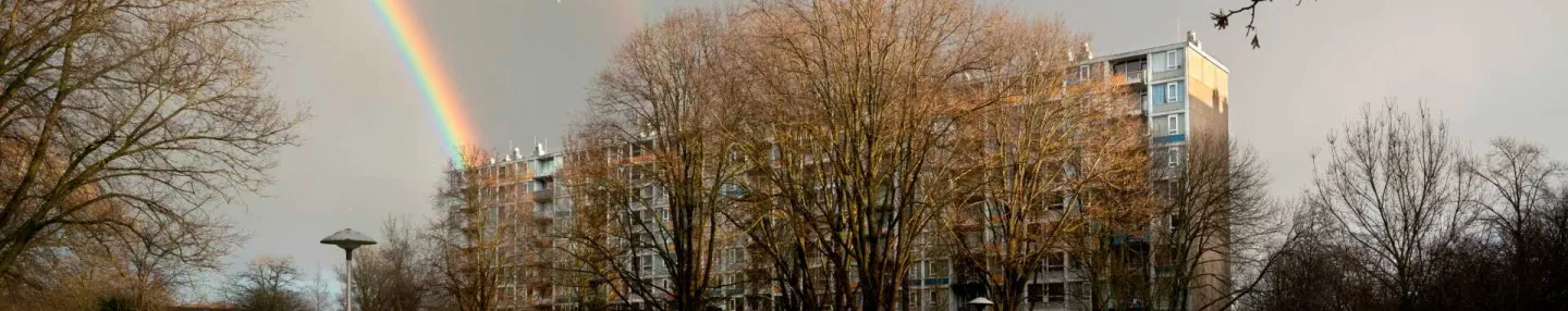 Flatgebouw in open omgeving, met regenbouw aan de horizon