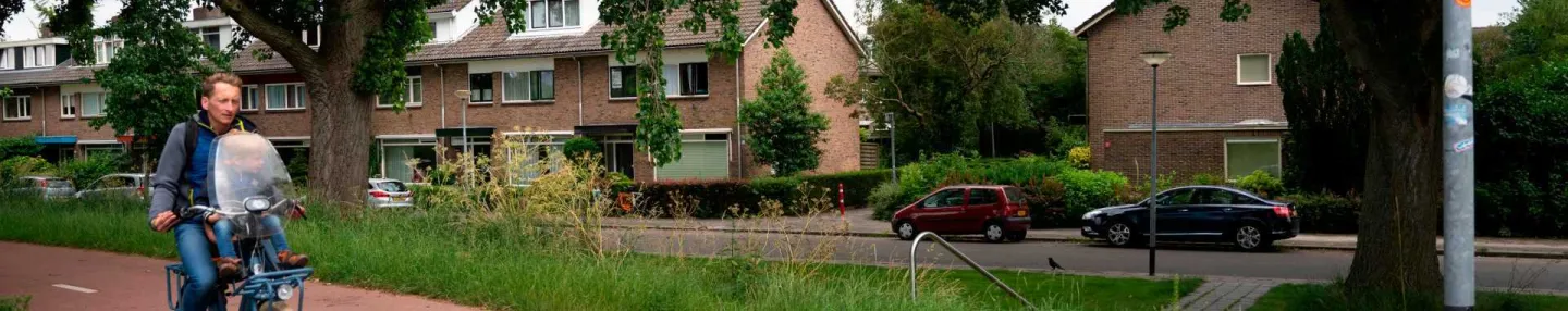 Fietsende man met kind in kinderzitje op fietspad in wijk met rijwoningen