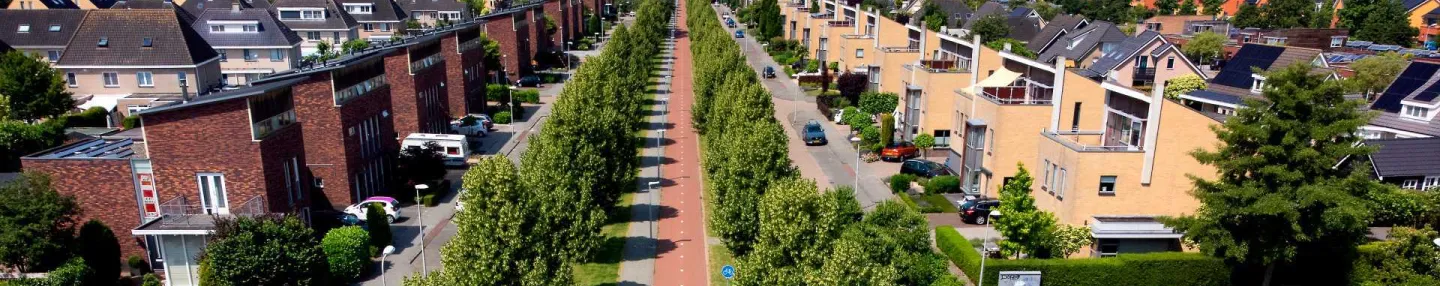 Een doorgaande weg met fietspad doorkruist een woonwijk met vrijstaande huizen