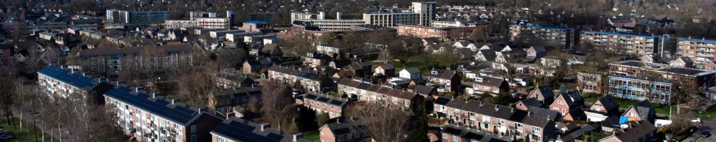 Luchtfoto met naoorlogse meerlaagse woningen in een wijk met veel bomen zonder blad