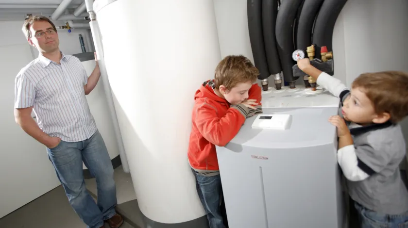 Twee kinderen kijken naar een nieuwe warmtepomp terwijl hun vader toekijkt.